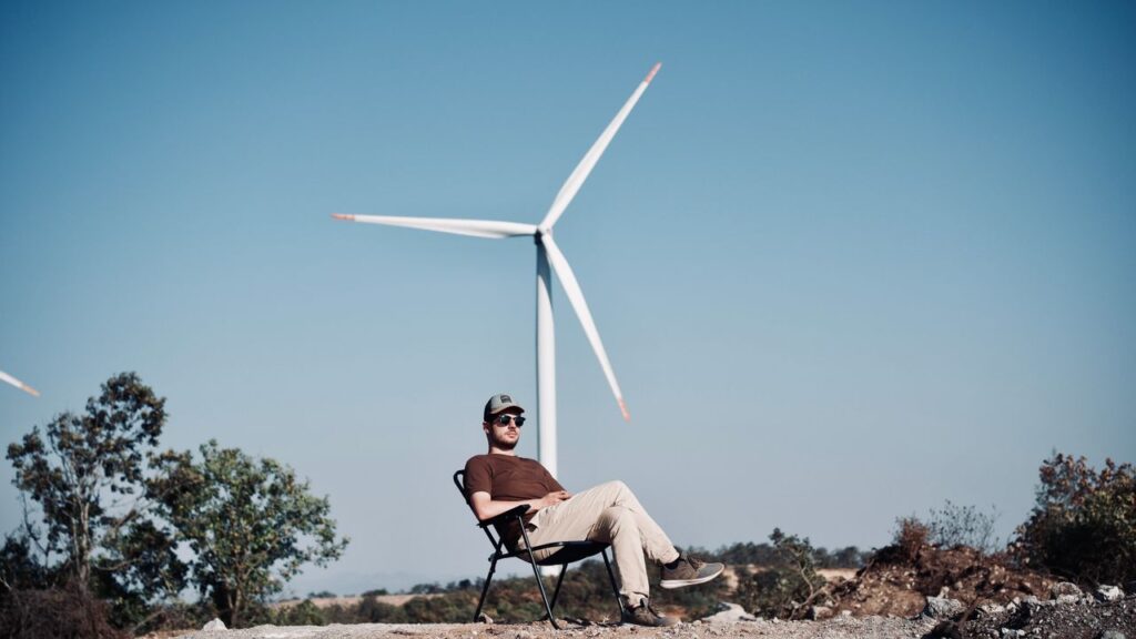 Man sitting on a chair by a wind turbine outdoors on a sunny day.